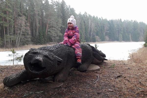 Nature Energy Trail and a wolf fishing with a tail from an Estonian folk tale. A happy little girl is sitting on the wolf's wooden sculpture