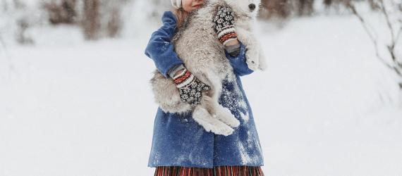 Tyttö seisoo lumisessa maastossa koira sylissään.