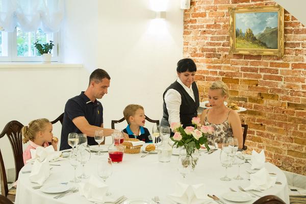 Saka kartanon ravintolan holvikellarisalissa illallista nauttiva perhe