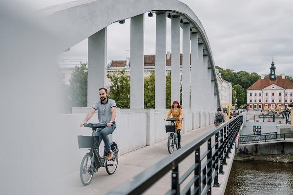 Arch Bridge in summer and young people riding bicycles of the Tartu bike sharing circuit