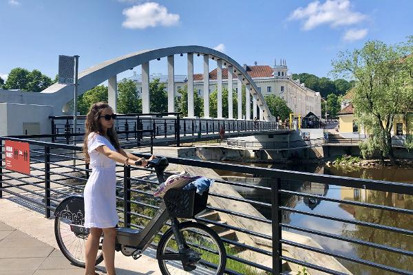 Die Bogenbrücke und eine Jugendliche mit einem Rad des Tartuer Fahrradverleihs daneben stehend