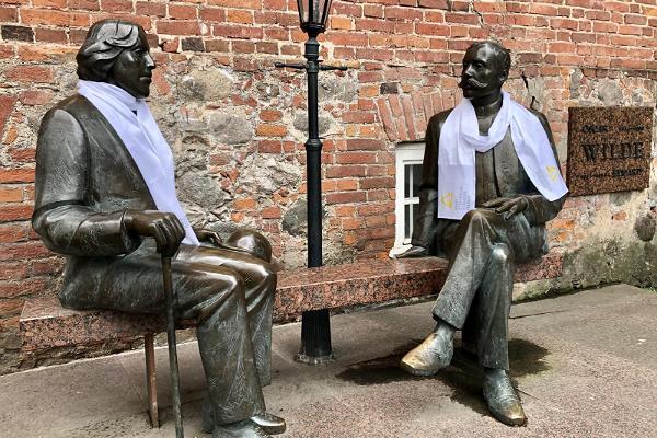 Två män, Eduard Vilde och Oscar Wilde sitter på en bänk av sten och pratar