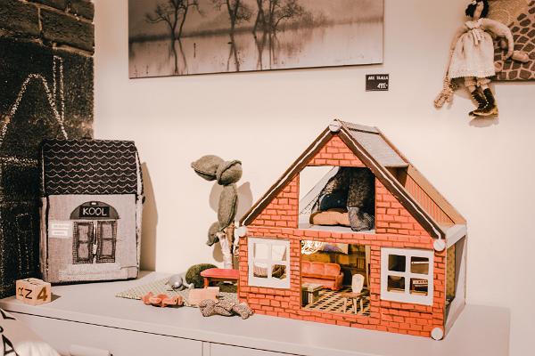 Studio shop Karud ja Pojad playroom: miniature bearhouse and textile schoolhouse, small bears, and a doll. A black-and-white photo of trees and the Emajõgi River on the wall.
