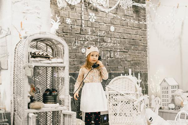 Studijas veikala "Karud ja Pojad" iekšskats: rotaļu istaba baltā ziemas noskaņā, maza meitene ar princeses kroni runā pa veclaicīgu telefonu ar vadu.
