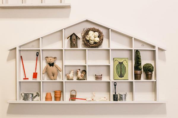 Studio shop Karud ja Pojad, tiny house-shaped shelf with miniatures, bird's nest, birdhouse, small bear, tiny rake and shovels, rooster, chicken, beetle painting, textile potted plants, bucket, watering can, flower pots