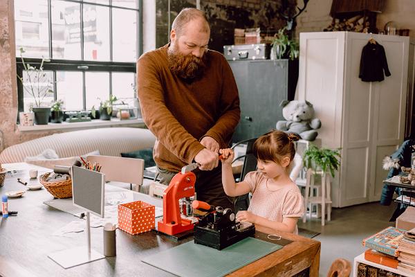 Vectēvs un mazmeitiņa, maza meitene, izgatavo nozīmīti studijā-veikalā "Karud ja Pojad" ar sarkanu nozīmīšu izgatavošanas mašīnu