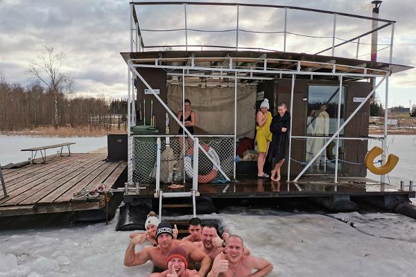 Saunagänger genießen ein Bad im Eisloch, im Hintergrund das Saunafloß auf Saadjärv