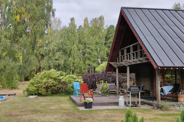 Den soliga terrassen där du kan grilla på Marknagårdens semesterstugas bastuhus. Framför terrassen finns det en lekstuga och en sandlåda för barn. 
